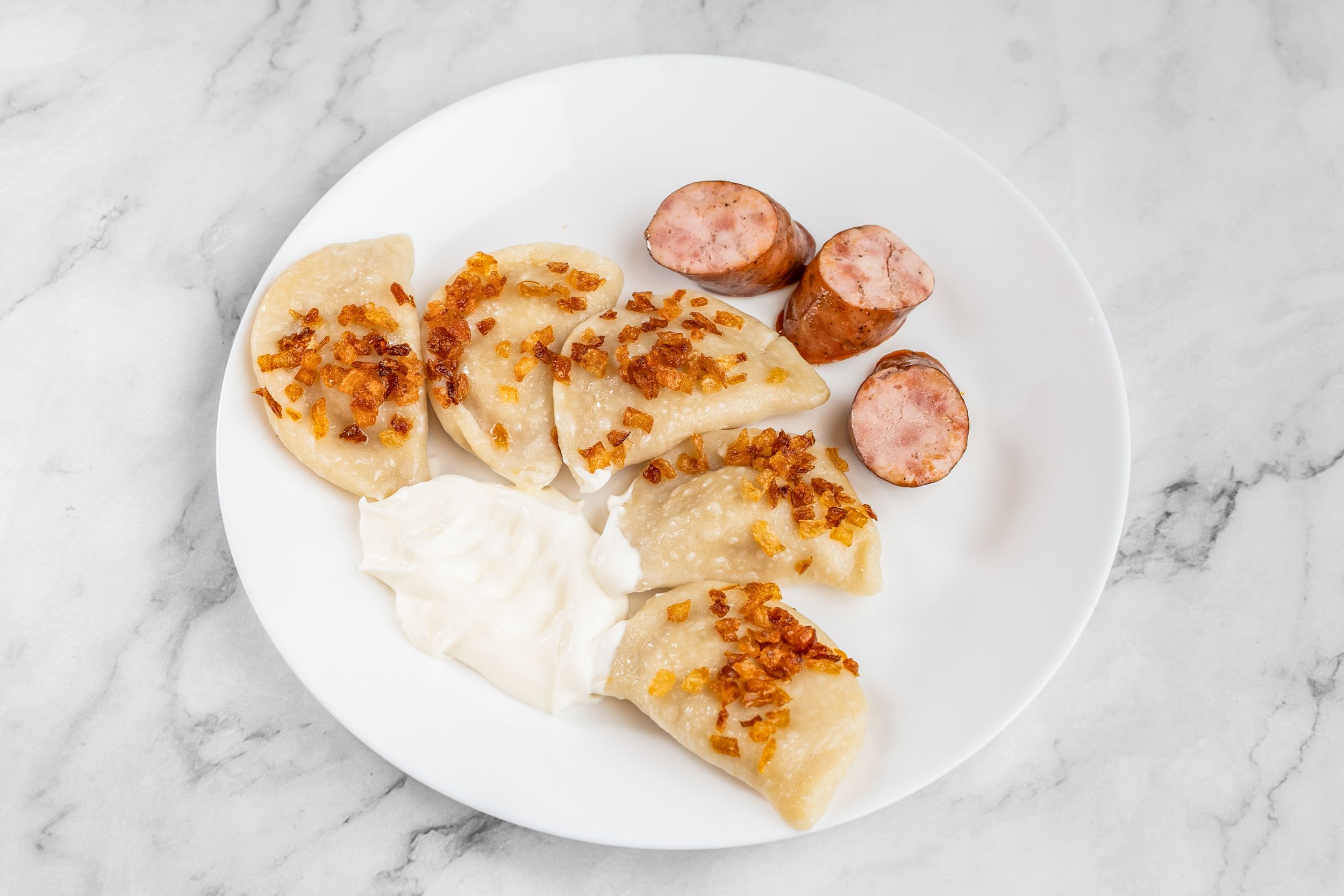 A plate of DONYA perogies with fried onions, kovbasa and sour cream
